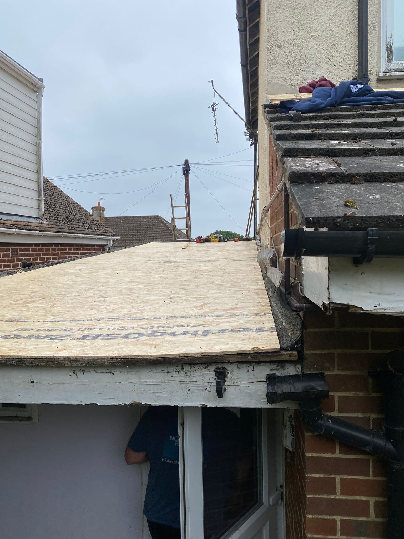 A new timber deck laid on a small flat roof against a brick wall, with black guttering beside it