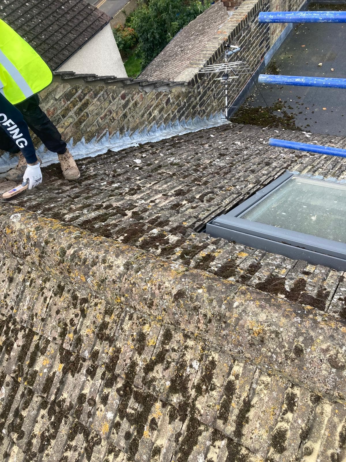 Working along the ridge of a concrete tiled roof from the scaffold, beside a roof window