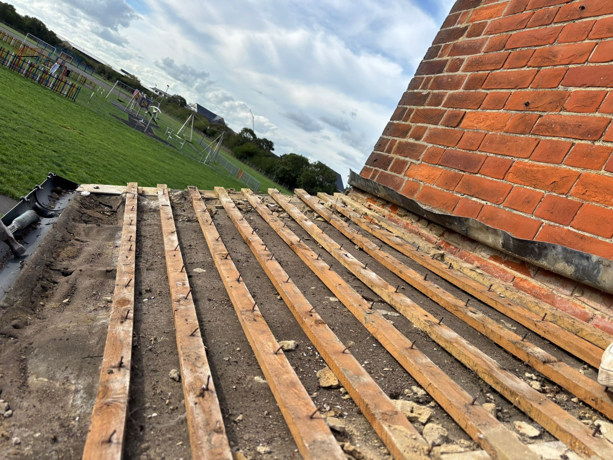 A roof stripped back to the battens, with open farmland behind it