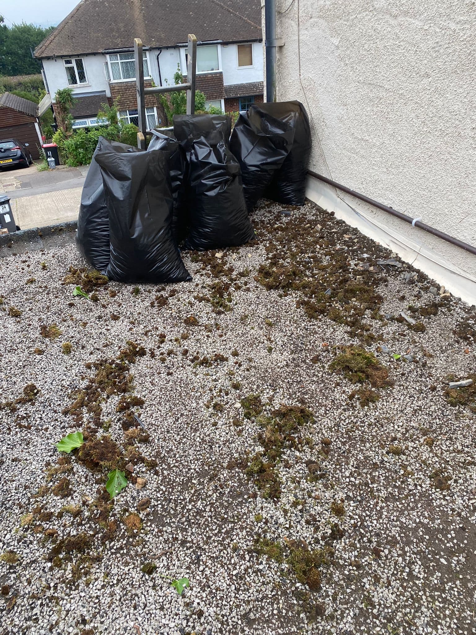 An old flat roof covered in chippings and moss, with the cleared debris bagged up