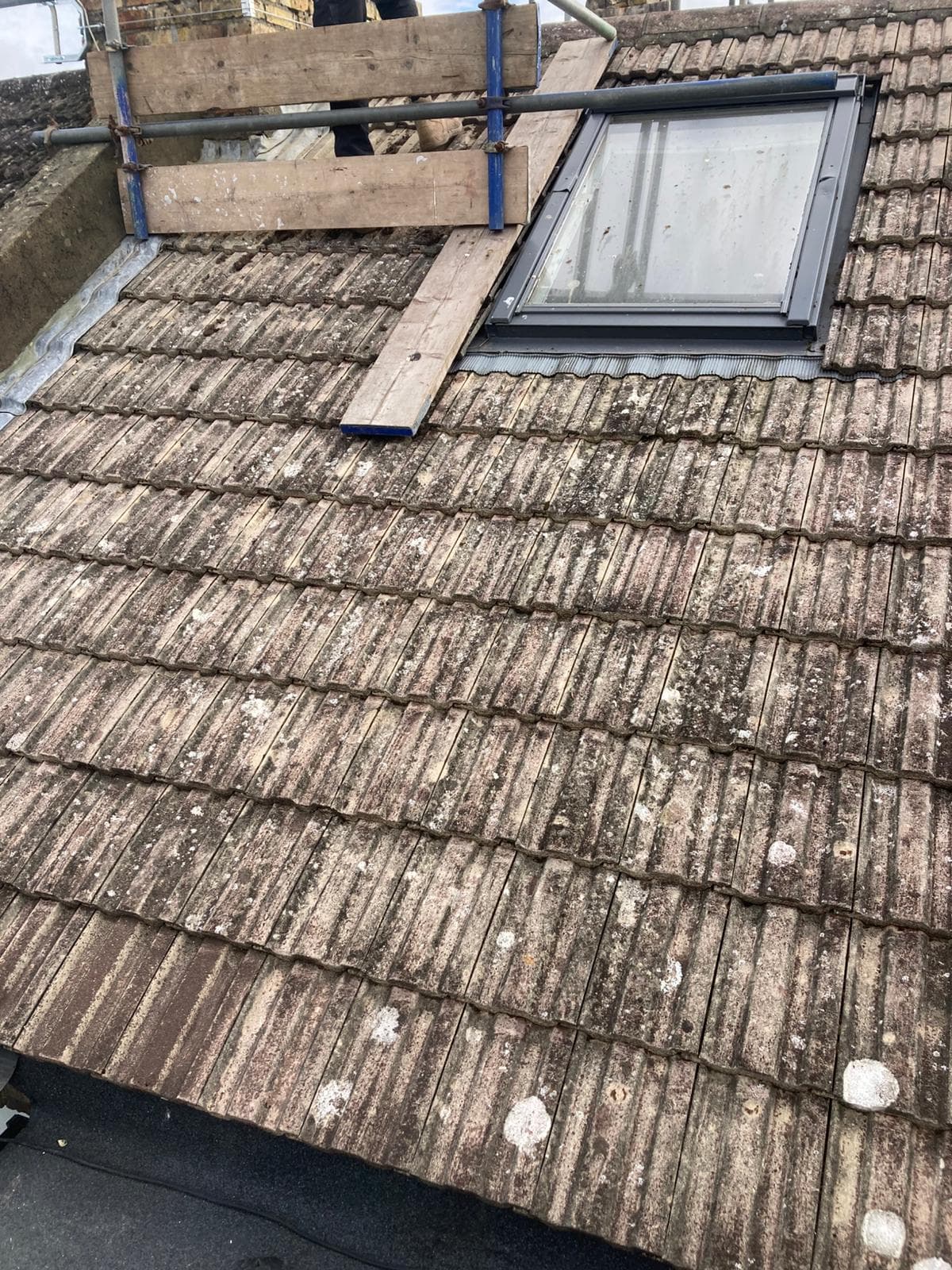 A roof window in a concrete tiled slope, with boards laid on the scaffold beside it
