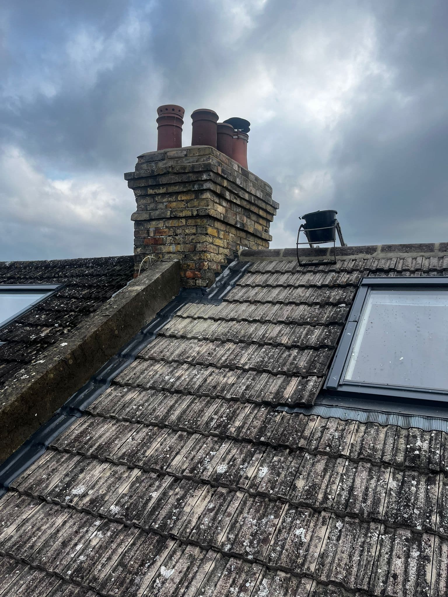 A tiled roof with two roof windows below a brick chimney stack