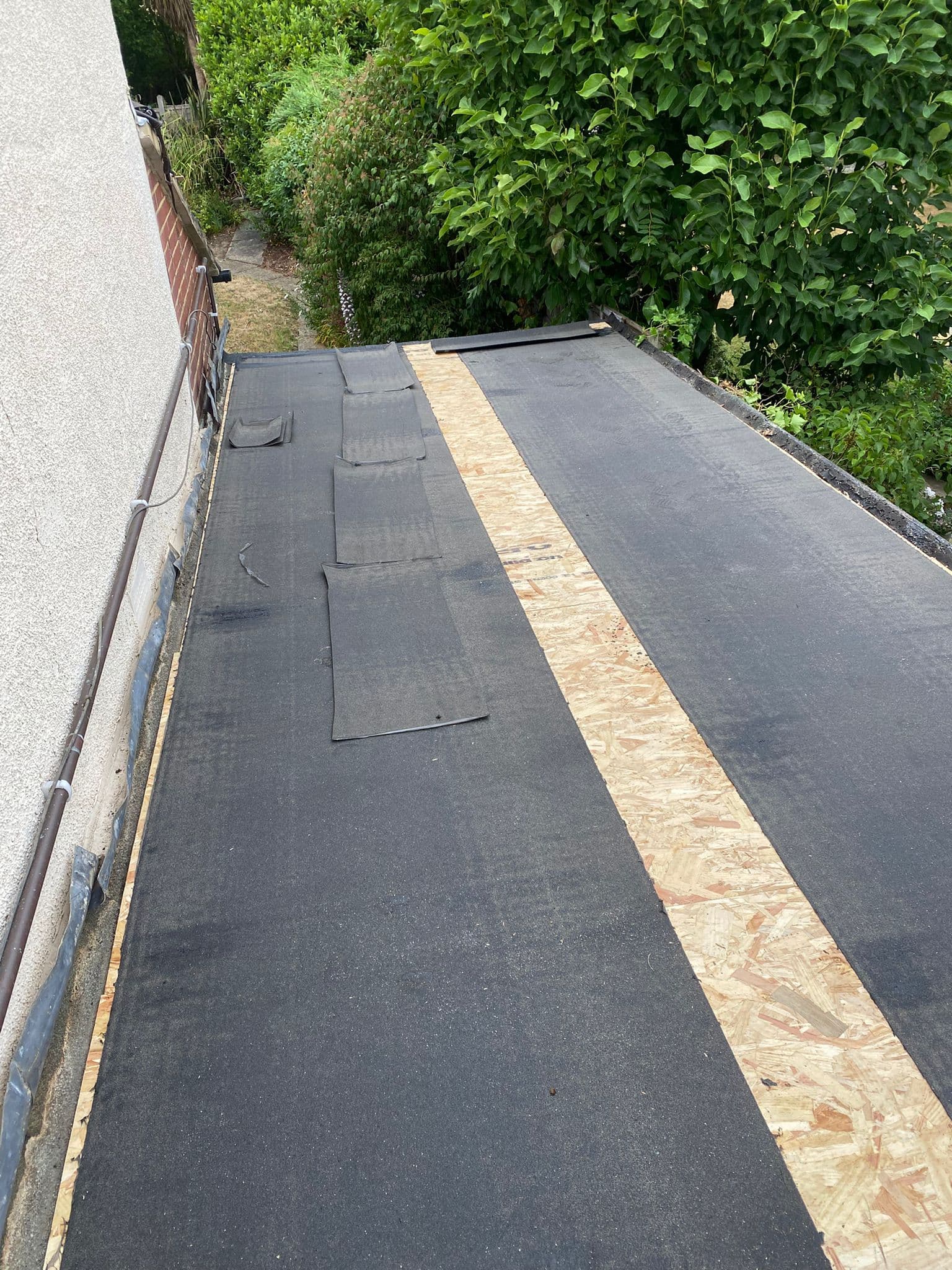 A flat roof being covered, with new membrane laid over timber boards beside a garden