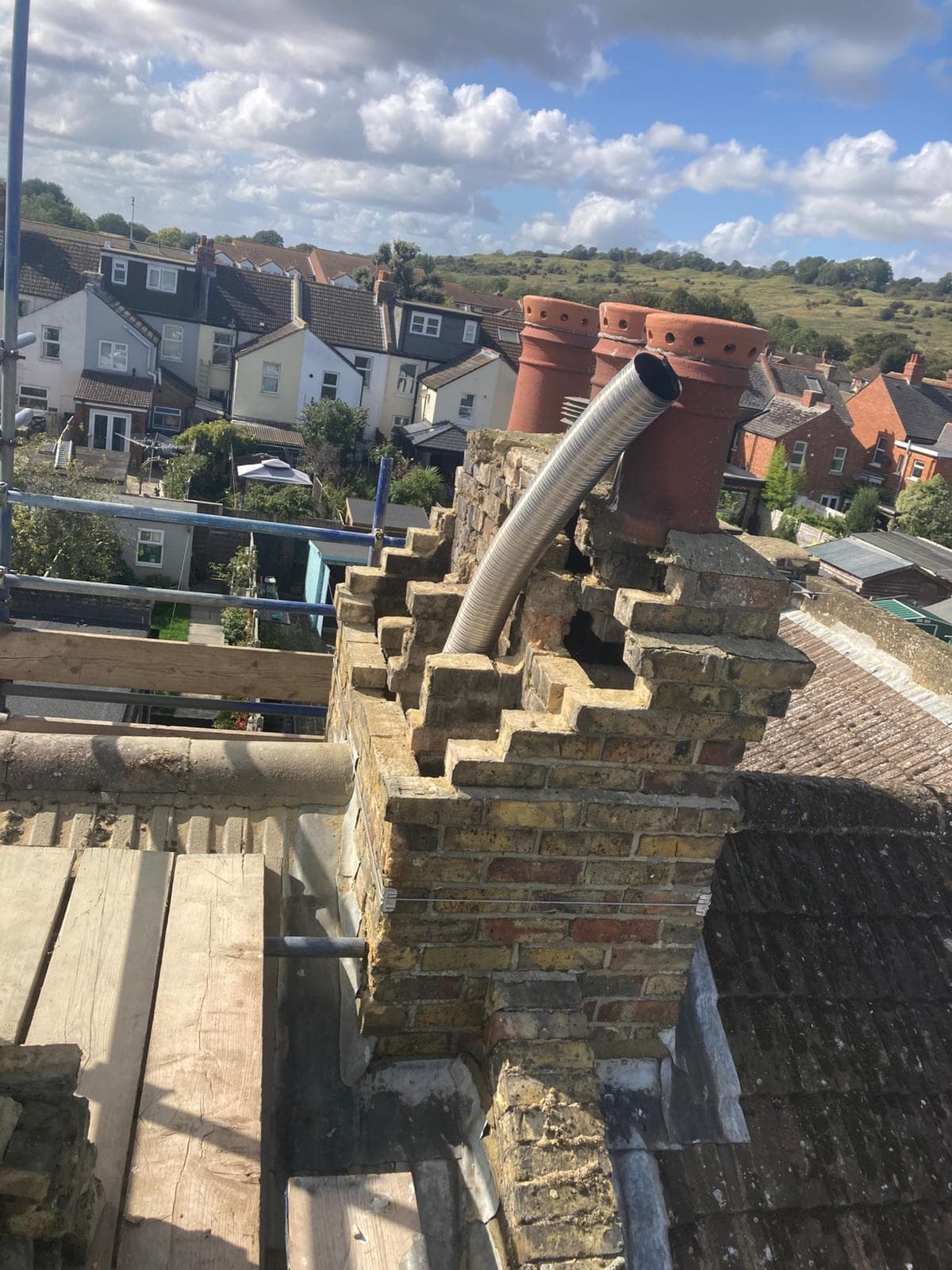 A chimney stack being rebuilt from a scaffold, with rooftops behind