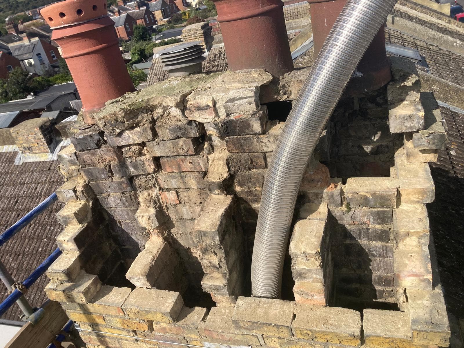 A brick chimney stack taken down part way for rebuilding, with a flexible flue liner rising out of it and clay pots behind
