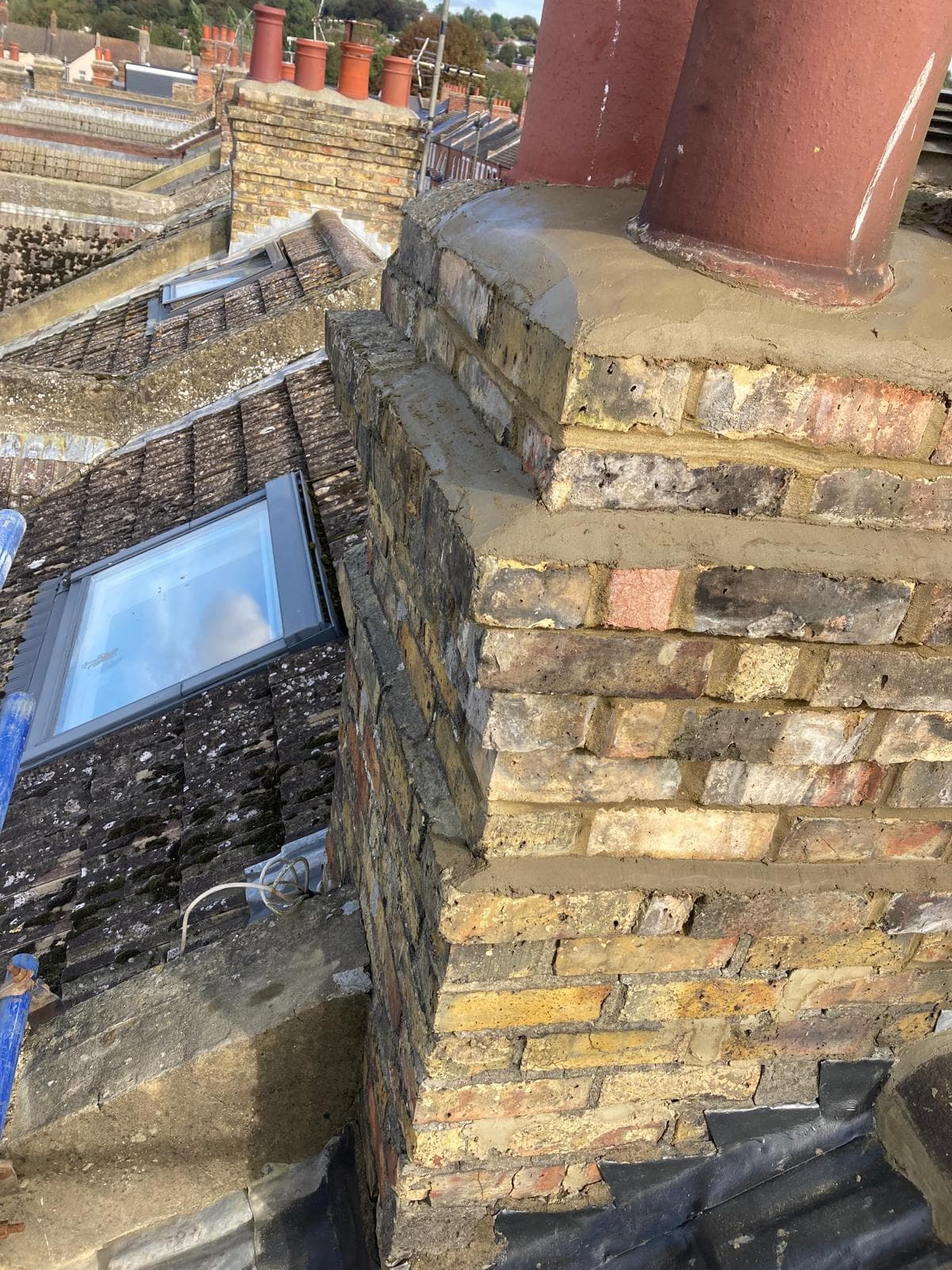 A repointed brick chimney stack with new flaunching, beside a roof window, with lead flashing at its base