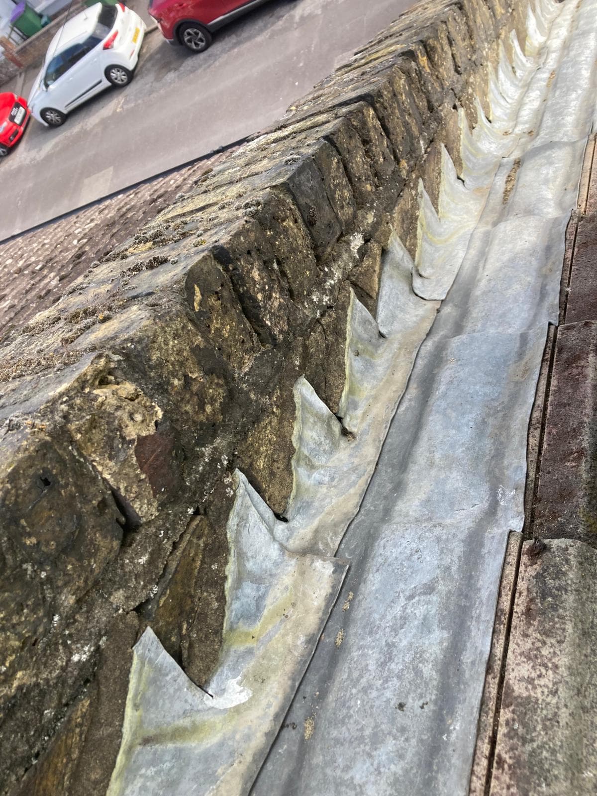 A lead gutter running along a stepped brick parapet, with lead flashing dressed up the brickwork