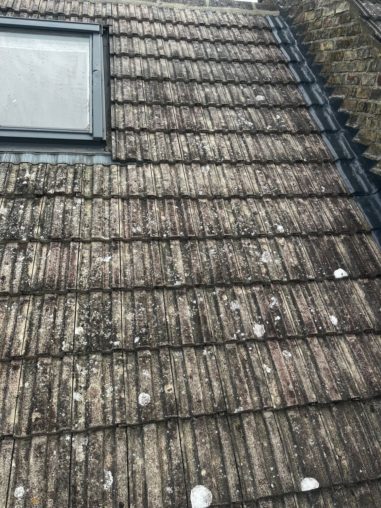 Weathered concrete tiles below a roof window, beside a brick party wall